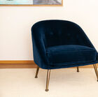 Un fauteuil aux accents Art déco modernisé associant coque arrondie, velours sombre et laiton.