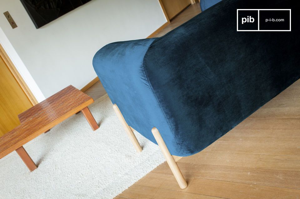 Le revêtement en velours bleu sombre contraste avec le bois clair du piètement.
