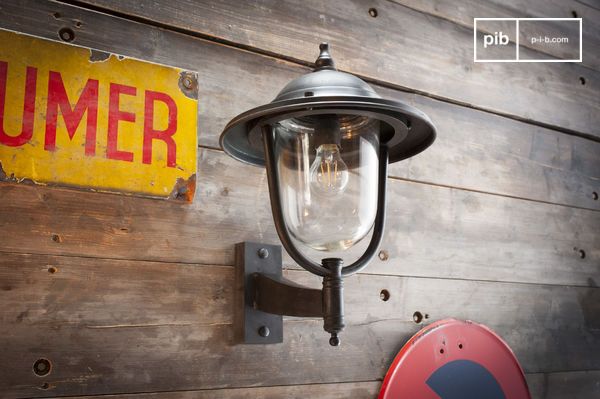 L'applique adopte une silhouette classique de lanterne murale, avec son abat-jour évasé et son diffuseur en verre clair qui lui confère un style intemporel