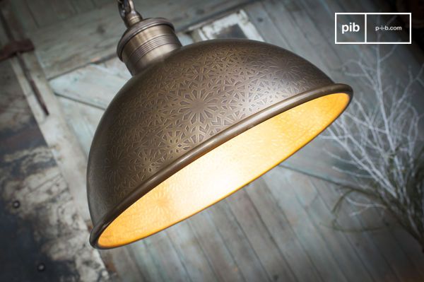 Une suspension qui présente un large abat-jour hémisphérique décoré de motifs ciselés, qui diffusent une lumière chaude et enveloppante.