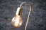 The long filament bulb is supported by a brushed golden brass rod.