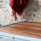 Le plateau en teck massif veiné apporte une touche de chaleur qui contraste avec le métal.