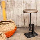Le tabouret associe une assise ronde en bois et un piètement en fonte noire qui évoque les meubles d'atelier d'usine.